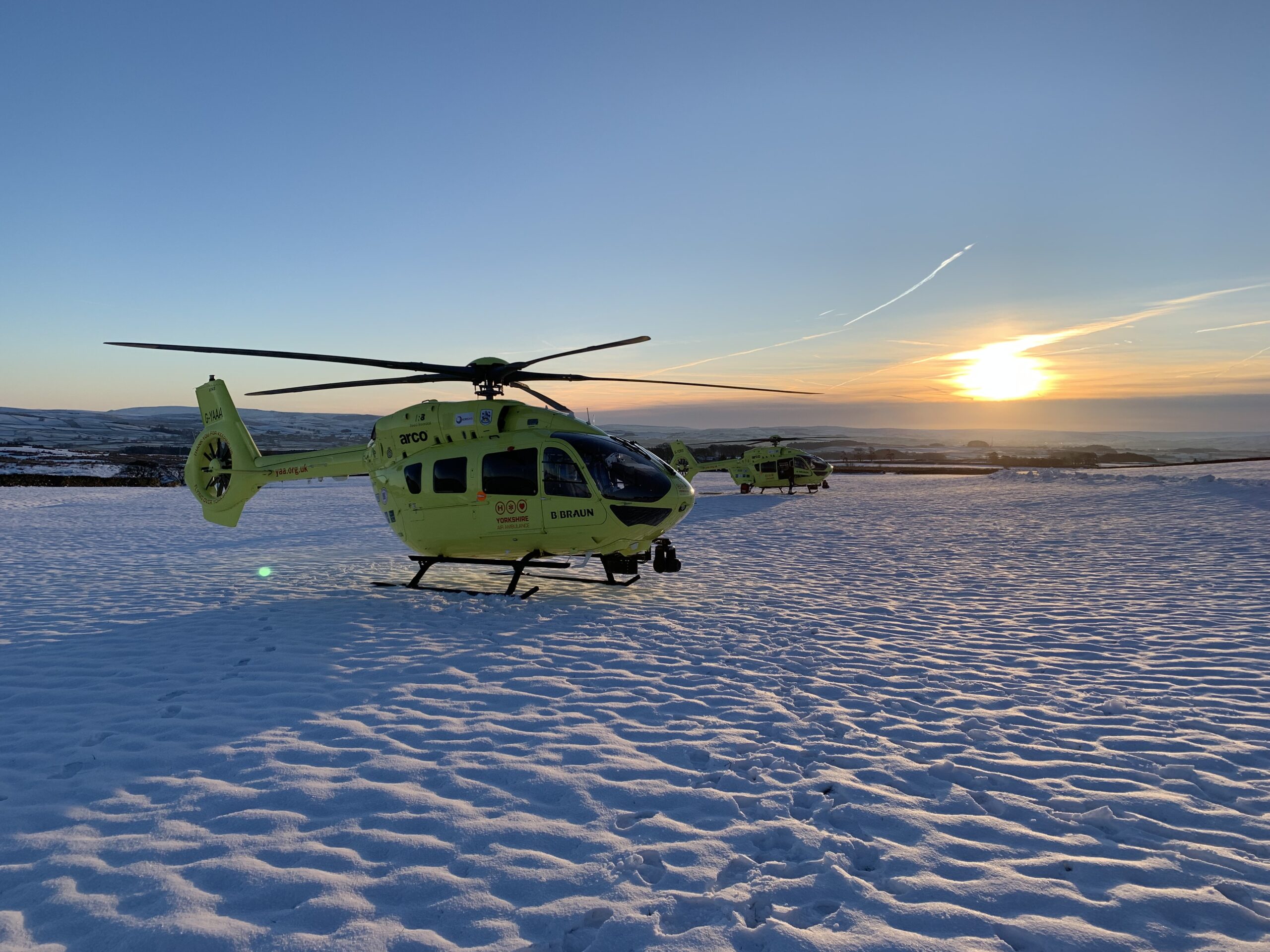 Two yellow helicopters in the snow at sunset