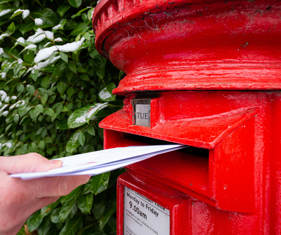 A persons hands posters letters into a red postbox