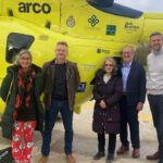 A group of people standing in front of a yellow helicopter.