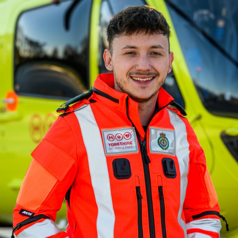 A man in an orange flight suit stood in front of a yellow helicopter