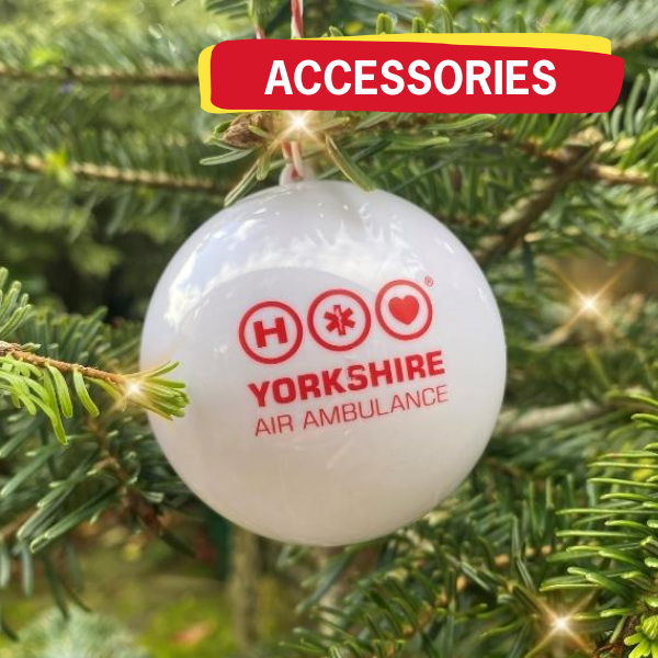 Close up image of a white ball with the red Yorkshire Air Ambulance logo hanging on a Christmas tree, with a graphic in the top right with the word 'ACCESSORIES'