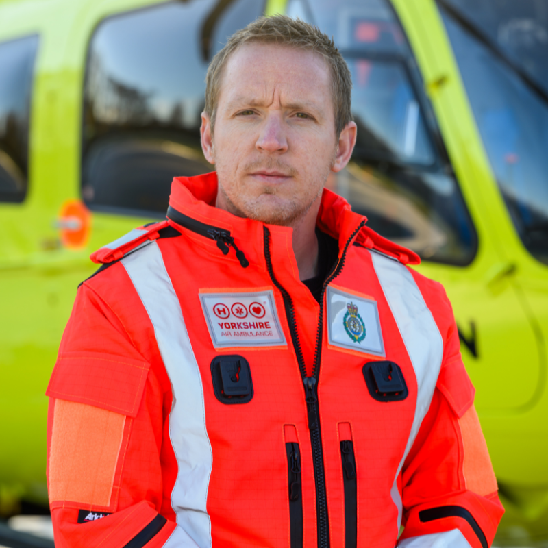 A man in an orange flight suit stood in front of a yellow helicopter